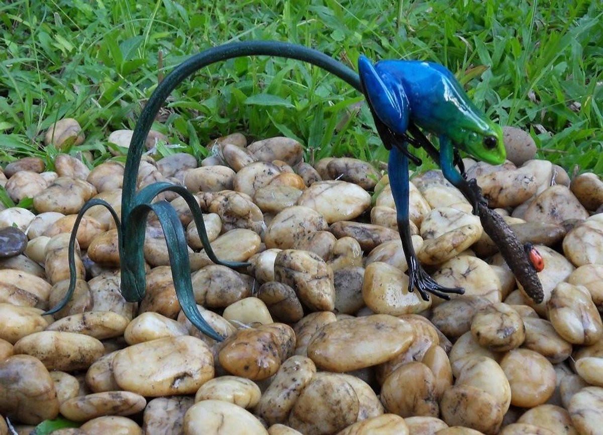 Brons beeld van een blauwe kikker aan een twijg voor op tafel